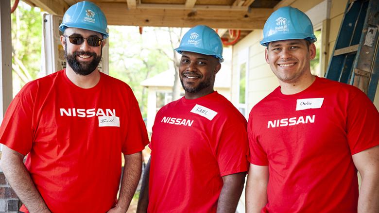 Three men in Nissan shirts smiling on build site.