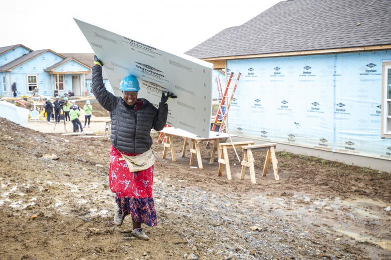 Noella carries a board of insulation above her head as she works on her home. 