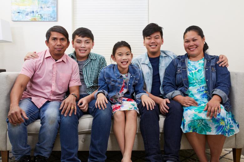 A family of two brothers, a sister, a mother and father pose for a portrait on the couch.