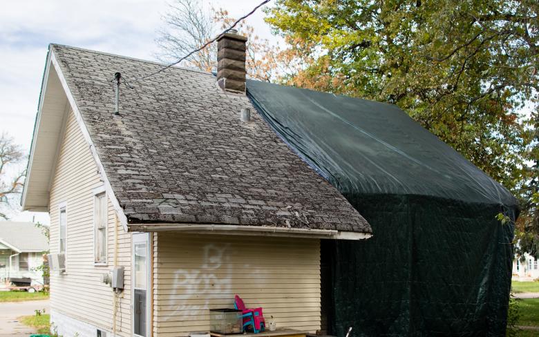 One-story house with tarp over half of it and graffiti