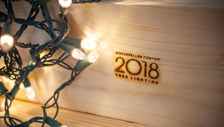 Lumber with "Rockefeller Center 2018 tree lighting" stamped onto it, surrounded by Christmas lights.
