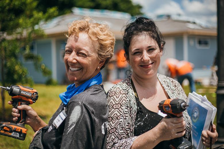 Two women holding drills and smiling on a build site.