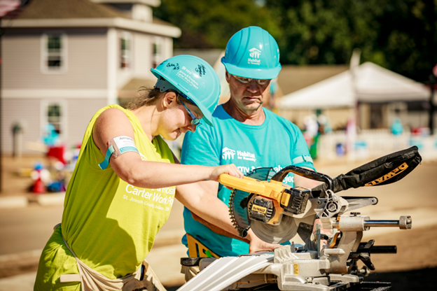 Two volunteers on a build site working with a saw.