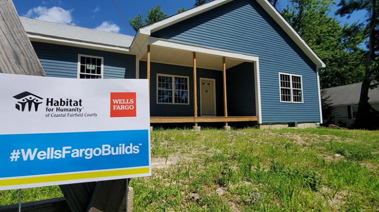 Blue house with a sign out front with Habitat for Humanity and Wells Fargo logos and #WellsFargoBuilds.
