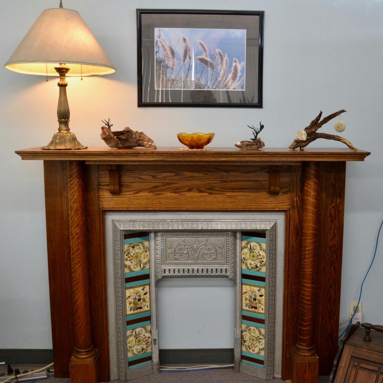 A golden oak fireplace with a painting hanging above it and trinkets on its mantel.