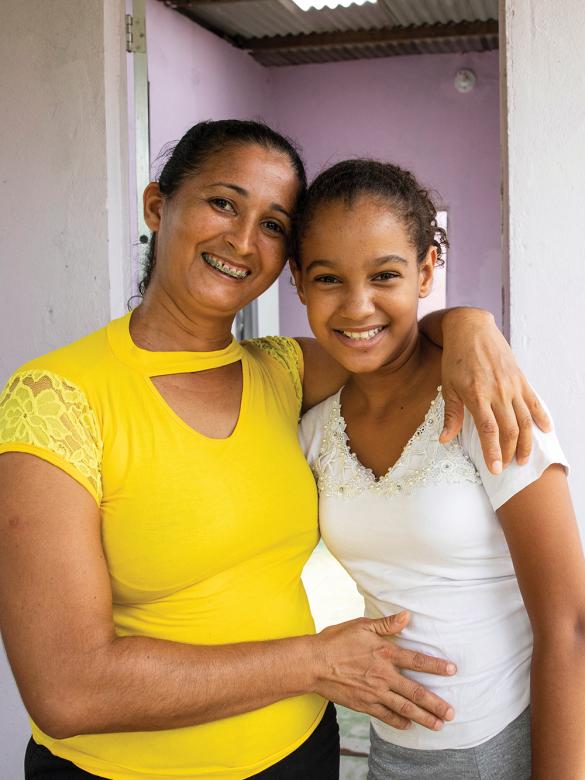 Mother in yellow top smiling with adolescent daughter in their home.