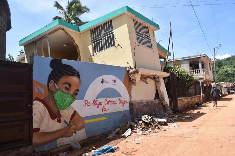 Photo: A mural of a woman in a mask next to a building and some rubble.