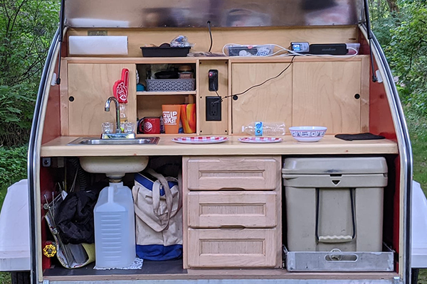 The back of a small camper with shelves, a sink and storage.