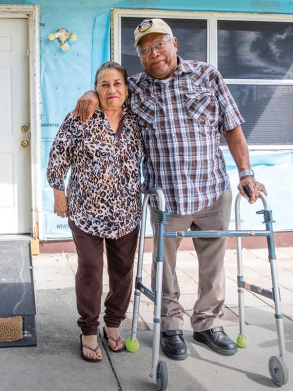Elderly man with walker and his wife standing in front of their home.