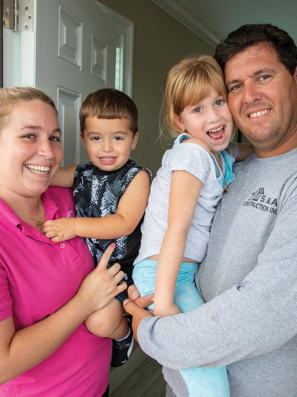 Parents holding two young kids standing in their doorway.