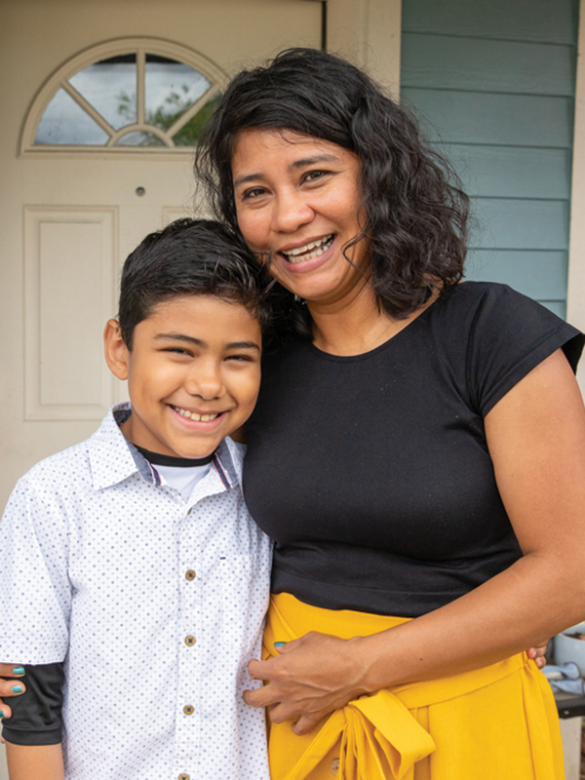 mother and young son smiling together in front of home.