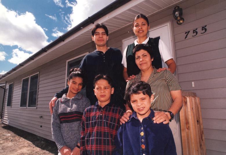 Maria and her five children standing in front of their grey home in 1996.