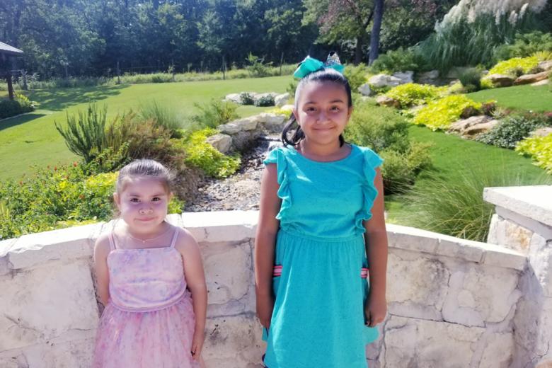 Dina's two young daughters stand together in a garden.