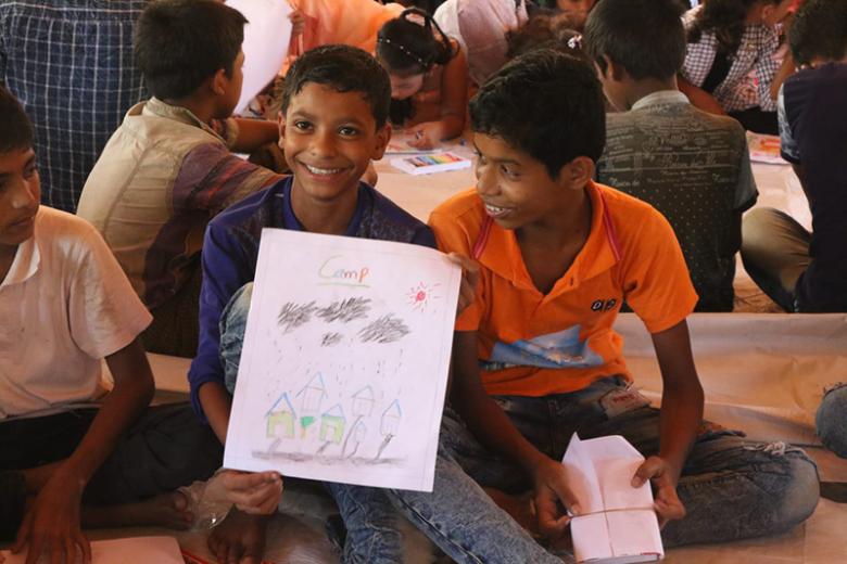 Young boy in Bangladesh refugee camp smiles as he shows off a drawing.