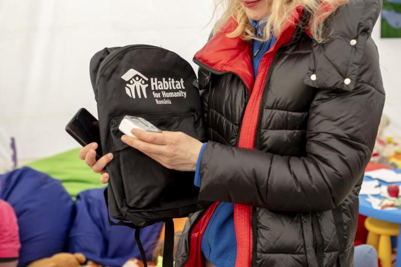 Woman holding Habitat for Humanity Romania backpack filled with supplies.