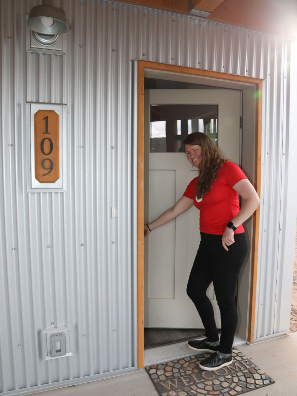 Smiling woman holding the front door to her home open.