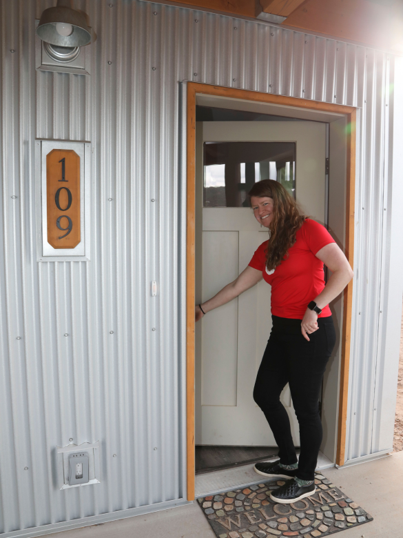 Smiling woman holding the front door to her home open. 