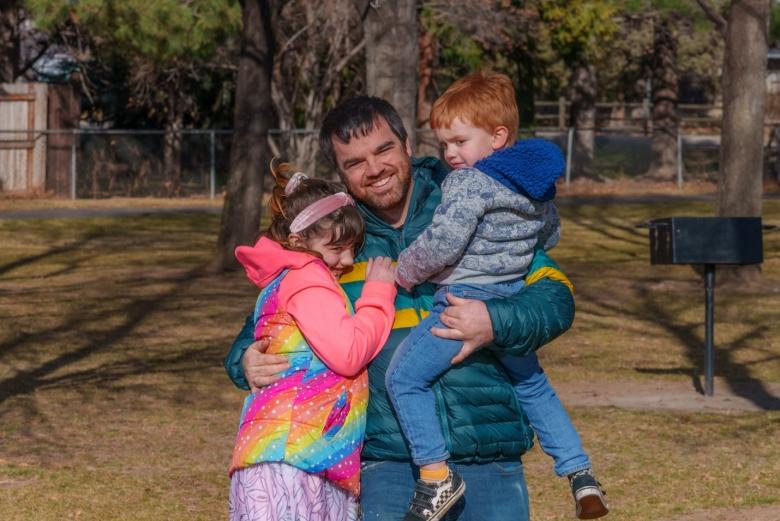 Photo of smiling man hugging his kids outside