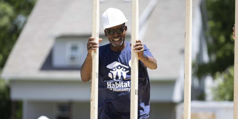 A man in a blue Habitat shirt and hard hat on a build site.