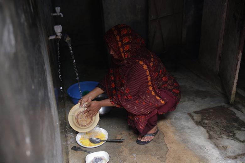Sumi washing dishes at the communal wash area next to her house