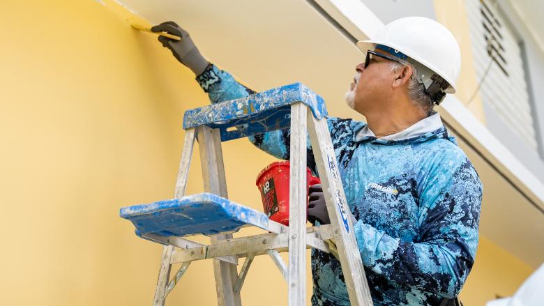 José on a ladder painting a home yellow