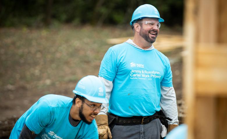 Garth Brooks in a blue volunteer shirt, smiling at someone across the build site.