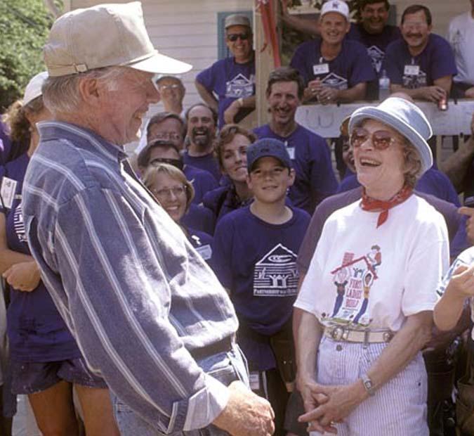 President and Mrs. Carter laughing together as they stand and talk with volunteers on a build site.