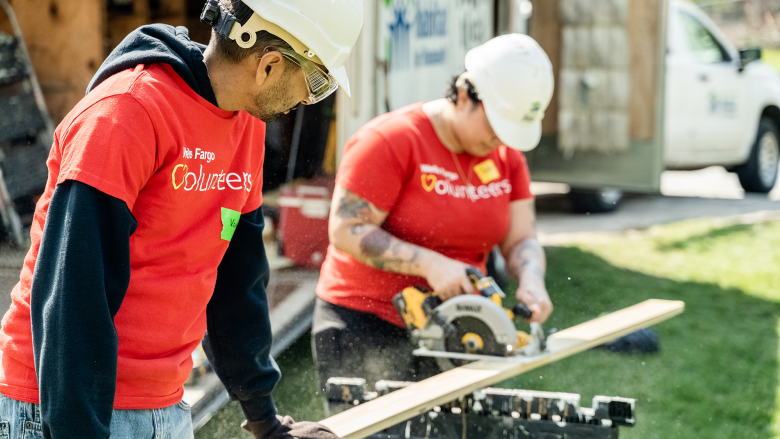 Two volunteers in red Wells Fargo shirts sawing wood.