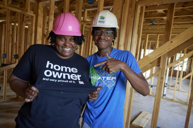Homeowner and her son smiling and wearing hard hats amid wood framing of their future home