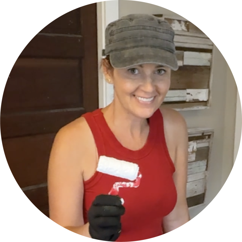 Woman in a red tank top and gray hat with a paint brush.