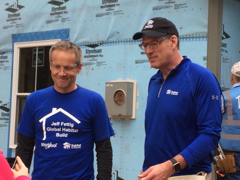 Marc Bitzer and Habitat CEO Jonathan Reckford stand together in dark blue Habitat shirts on a house construction site.