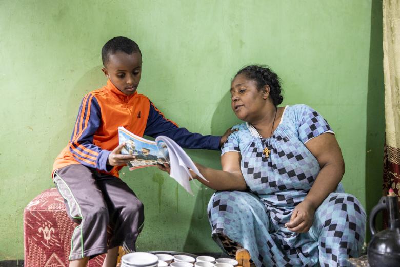 A lady helps her son with homework inside their home