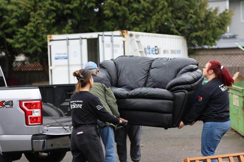 Three people lift a black leather couch off the bed of a gray pickup truck to donate to Habitat ReStore.