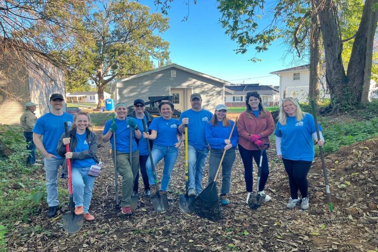 A group of volunteers in blue shirts pause and pose together in the yard during their build project.