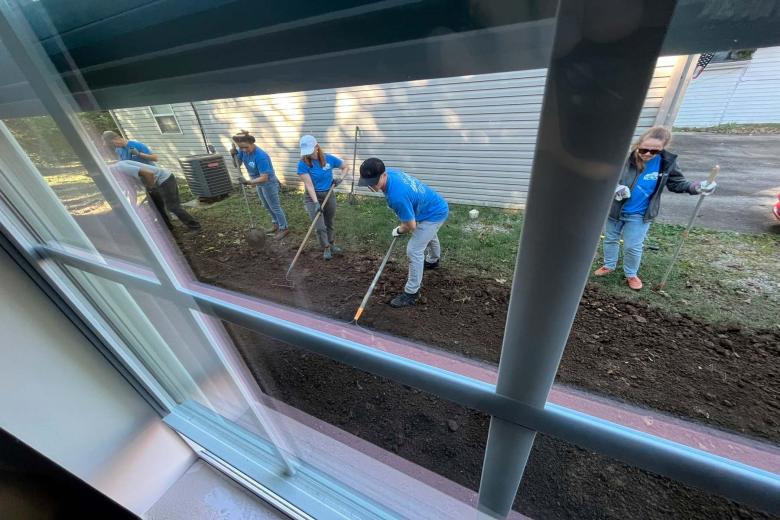 Volunteers work outside a house raking the yard.