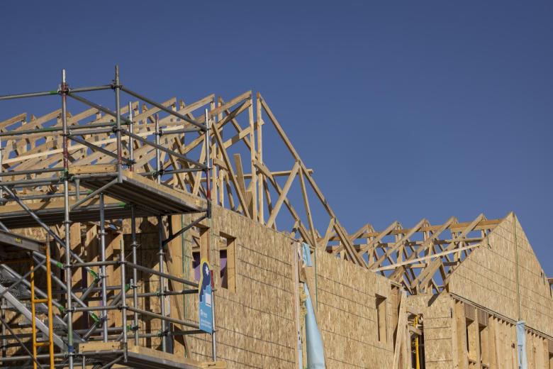 The wooden frame of roofs for Habitat houses is shown mid-build against a blue sky.