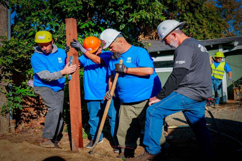 Four volunteers work on shoveling a hole in the ground to place a pipe.
