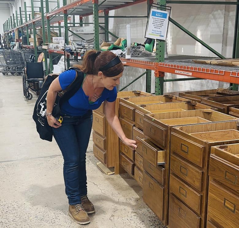Woman in blue shirt and jeans looking at cabinets. 