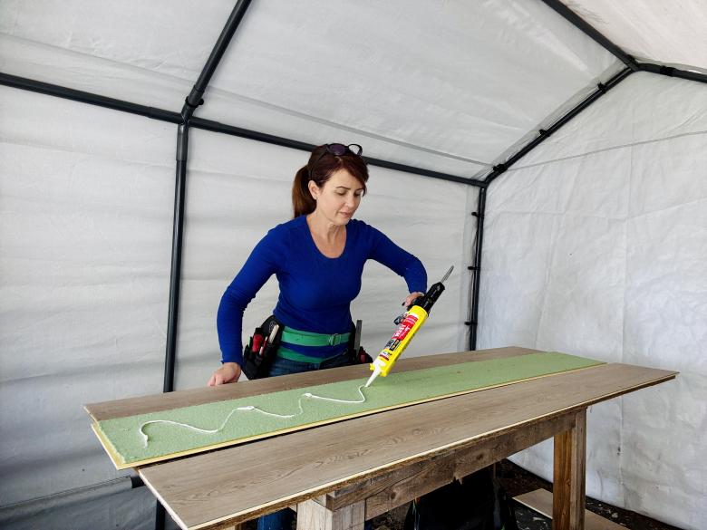 Woman in blue shirt gluing flooring to the stop of a desktop.