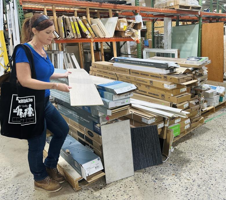 Woman in a blue shirt and jeans holding a flooring panel.