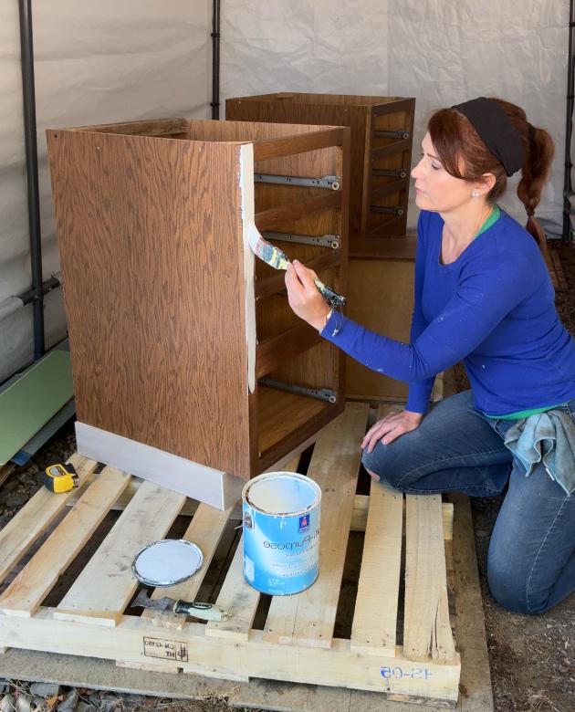 Woman in blue shirt applying primer to a brown cabinet. 