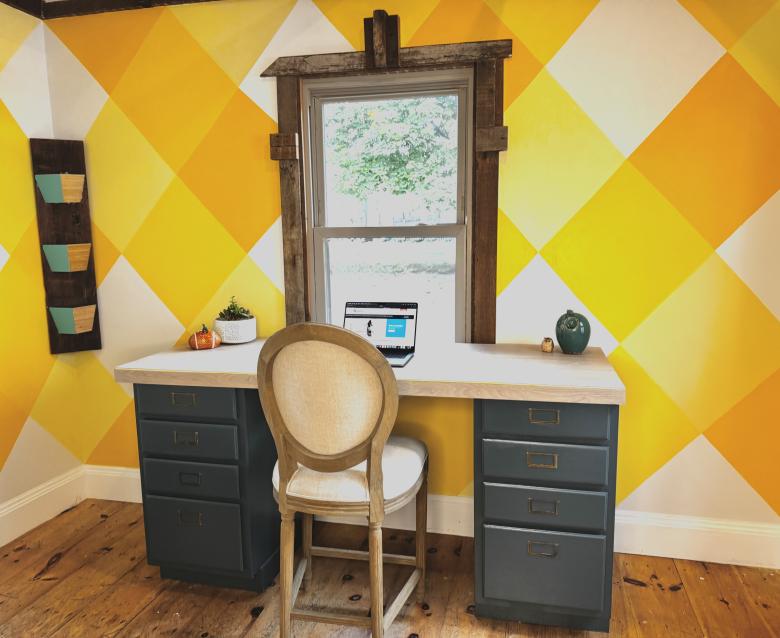 Blue cabinet desk with light-wash flooring desktop and chair in front of a yellow wall and window.