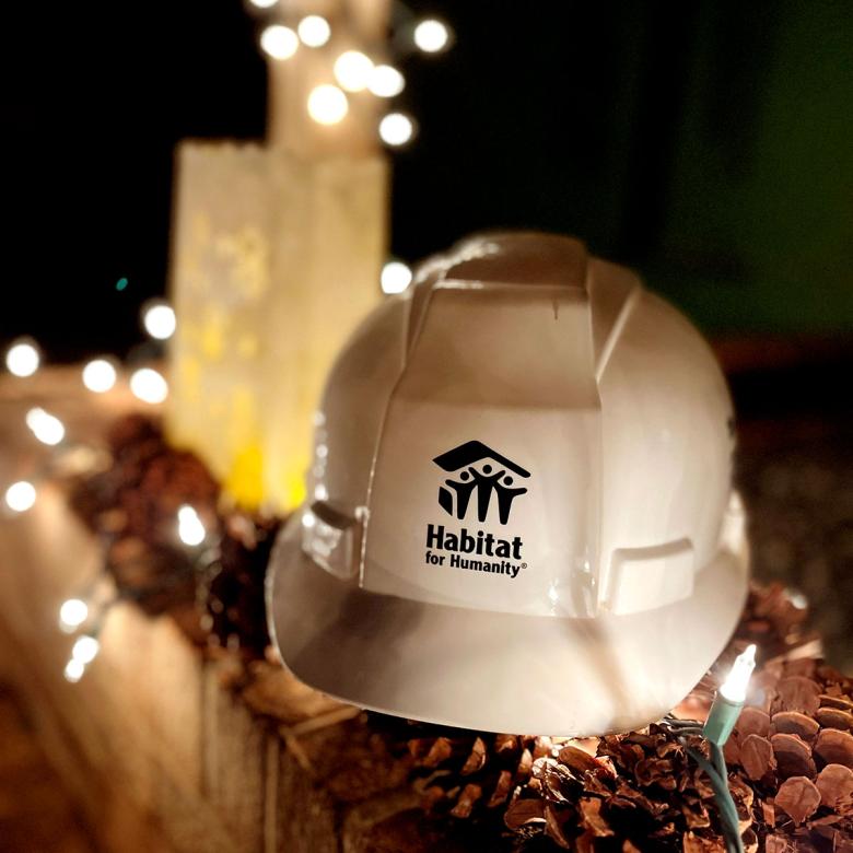 A white Habitat hard hat sittng on top of pinecones, surrounded by white string lights