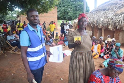 A man and woman standing in a rural setting with a group of people sat in the background