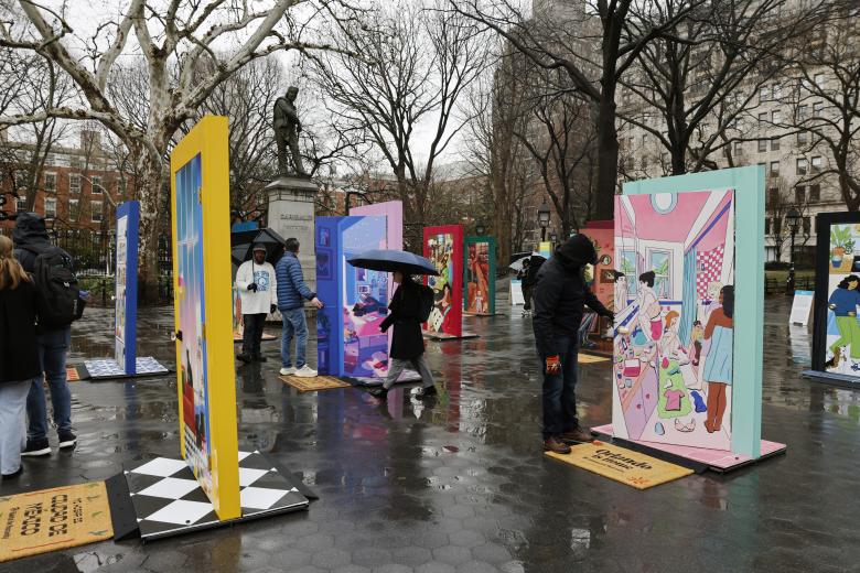 People walking through the Plaza in rainy weather looking at door art installations